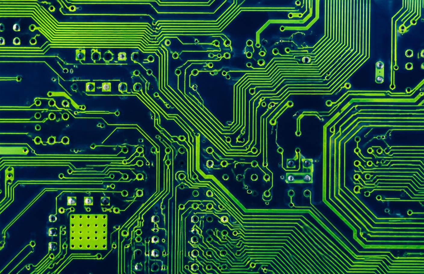 Close-up of a circuit board with bright green conductive traces over a dark blue substrate